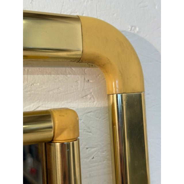 A striking vintage wall mirror featuring a bold brass frame accented with Lucite connectors at the rounded corners. The...