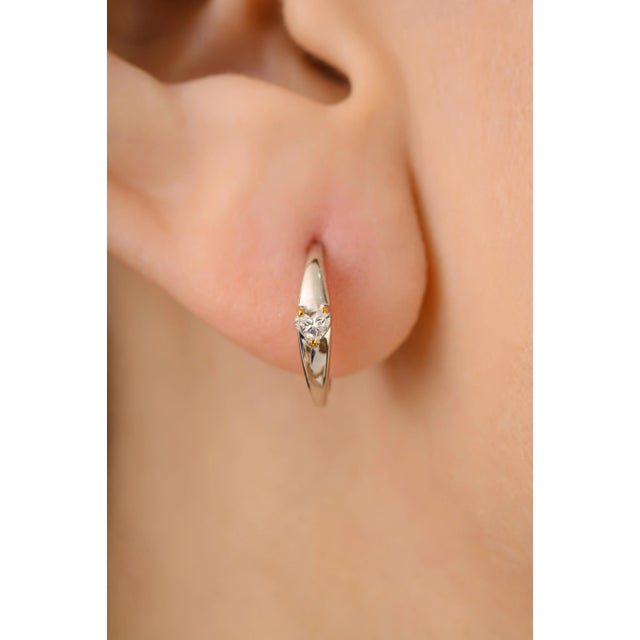 This 18K white and yellow gold hoop earrings featuring heart cut diamonds, 0.11 ct each. Diamonds are set in secure three-...