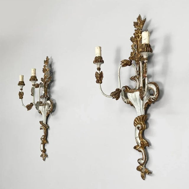 Italian two light wall lamps in wood with gold finish, 1700s Pair of gilded wood wall lamps. The lamp has two curved arms...