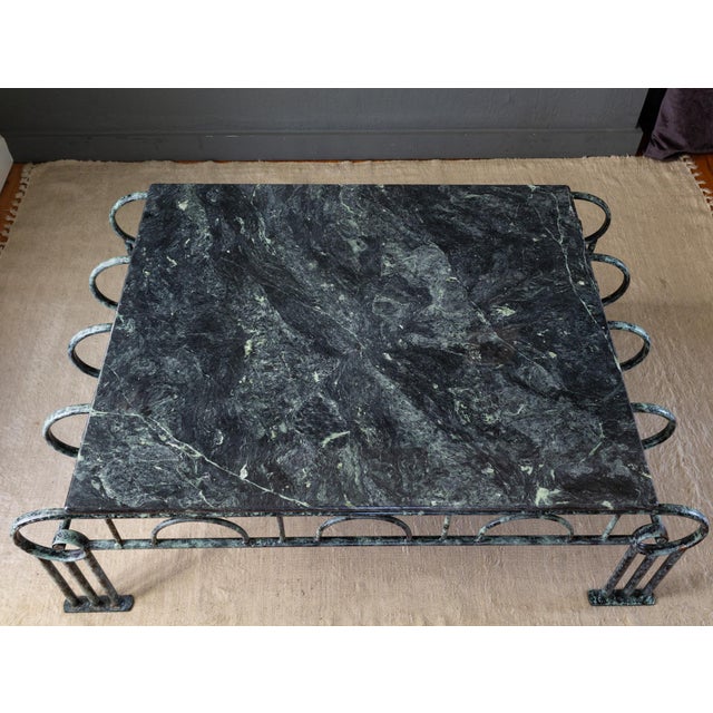 This sculptural coffee table features a deep, teal-green marble slab top on a curly, scalloped metal base with a faux...