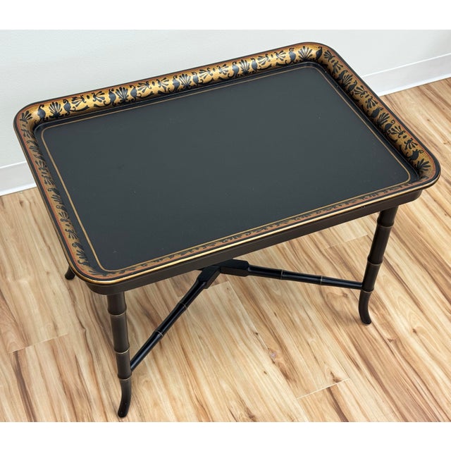 Vintage Regency style matte black metal tray table with gilt design to edge. Collapsible black base utilizes faux bamboo...