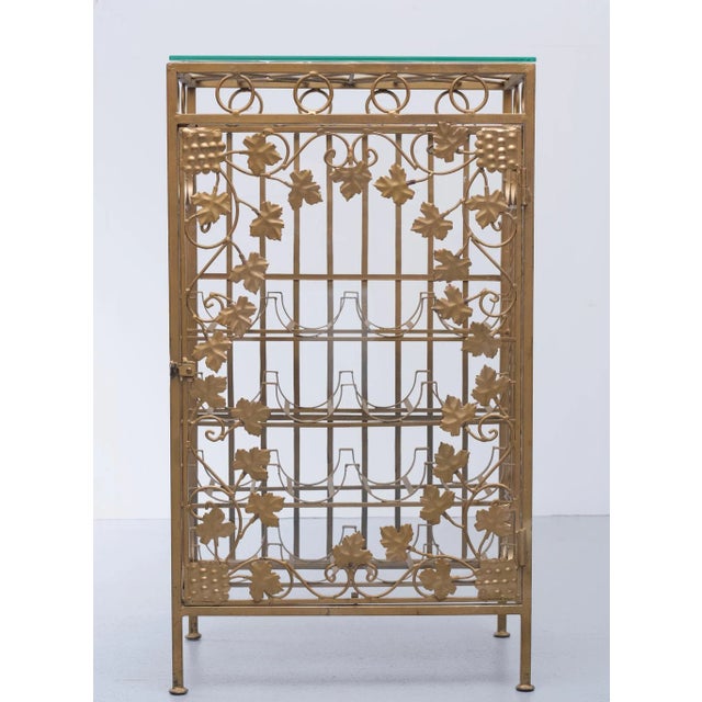 Gold metal wine rack decorated with leaves and ironwork. A thick glass top and a lockable glass door behind the door...