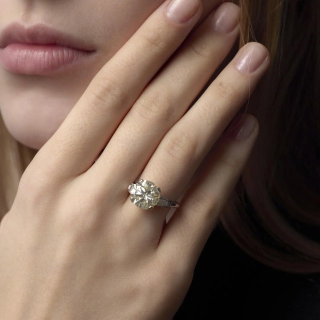 This Mid Century platinum ring showcases a breathtaking 5.07 carat diamond framed by elegant baguette accents, embodying...