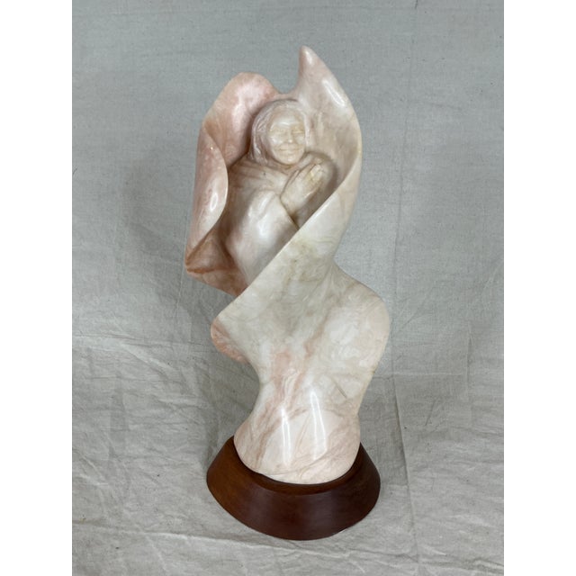 Carved pink alabaster sculpture depicting a Native American woman wrapped in abstract waves or flames. This sculpture was...
