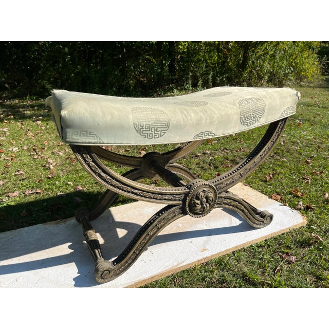 A single antique carved wood curule style stool or “x” bench with curved upholstered seat.