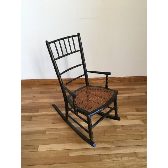 This is an antique child rocking chair made during the late 19th century in the aesthetic style. It is painted black with...