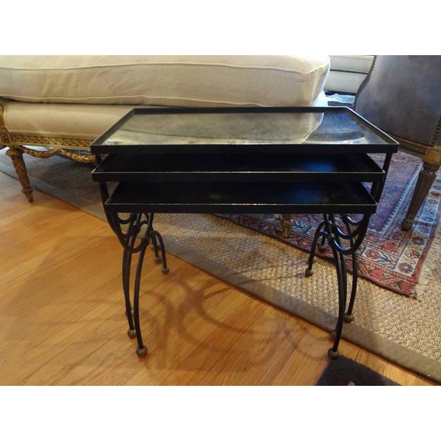 Versatile set of three French mid century modern iron nesting tables with brass accents and aged mirrored tops. These...