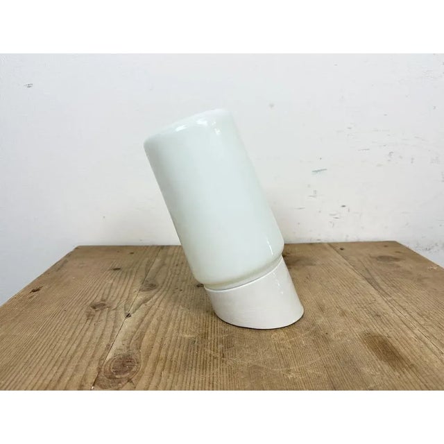 Vintage industrial light made in Poland during the 1970s.It features a white porcelain wall mounting and a milk glass...