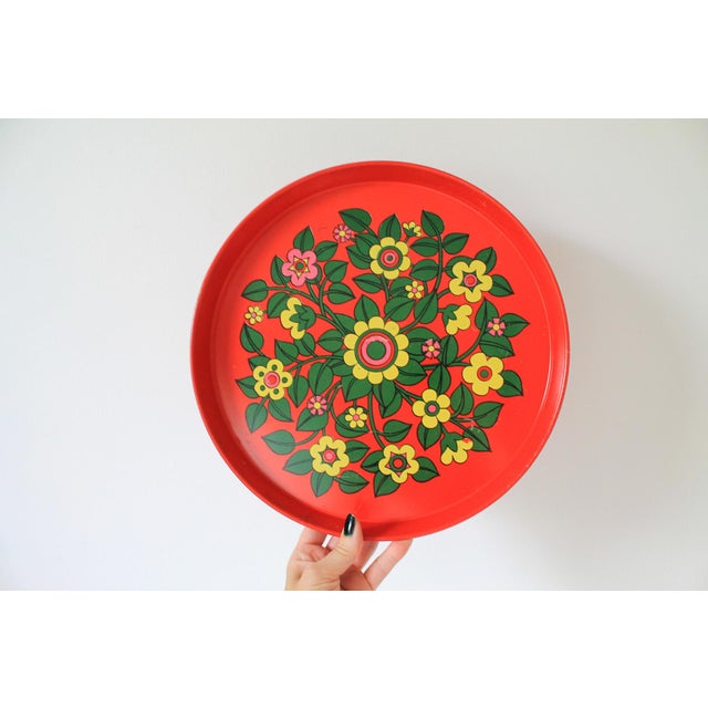 Vintage 1970s round red metal serving tray featuring a bright "flower power" floral pattern. The main color is an orangish...