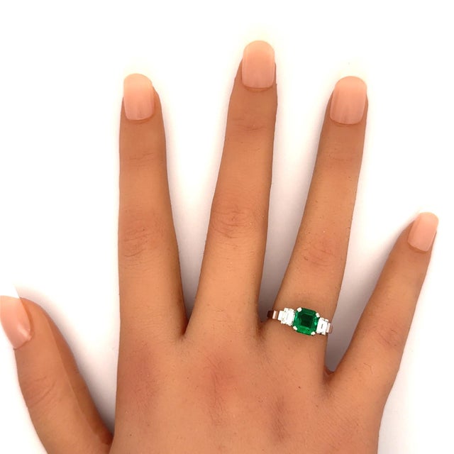 A striking emerald-cut emerald, weighing 1.26 carats, commands attention at the center of this classic three-stone ring....