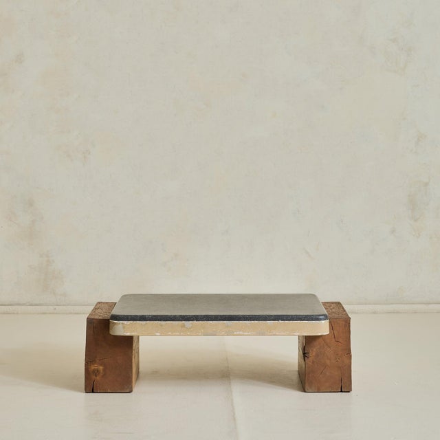 A 1970s Belgian coffee table, defined by the contrast between a honed slate top and solid wood block supports. The top is...