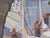 In "Skipper's Orders," a lively scene unfolds as sailors prepare their boats under the dappled shade of a tree. The use of...