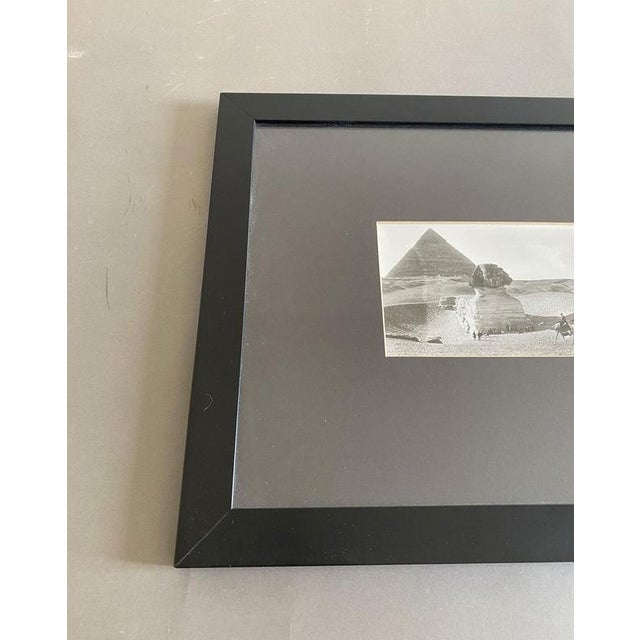 This captivating black-and-white photograph depicts a couple of desert Bedouins, captured in front of the Pyramid and the...