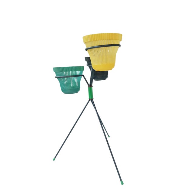 A lightweight, geometrically designed vintage plant stand, composed of a lacquered metal tripod structure that supports...