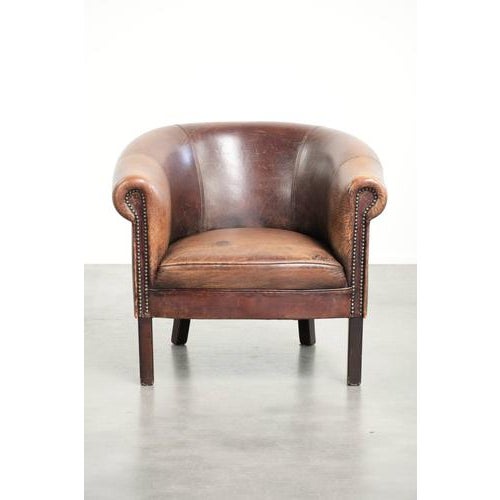 This lovely sheepskin club armchair features a beautiful patina, a subtle size, and a vintage appearance. It has a fixed...