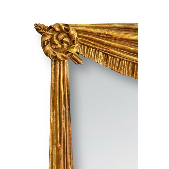 A large and striking giltwood Italian wall mirror featuring a finely carved drapery motif. A swag trimmed in fringe spans...
