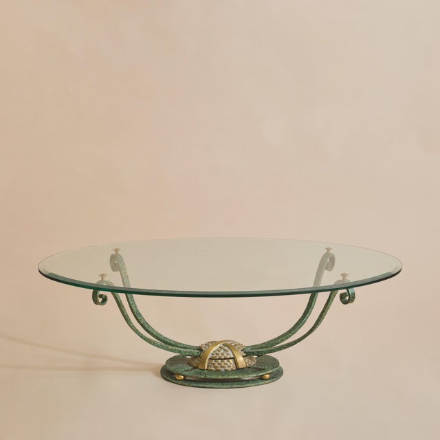A French oval coffee table from the 1980s with a beveled glass top appearing to float above a sculptural iron and bronze...