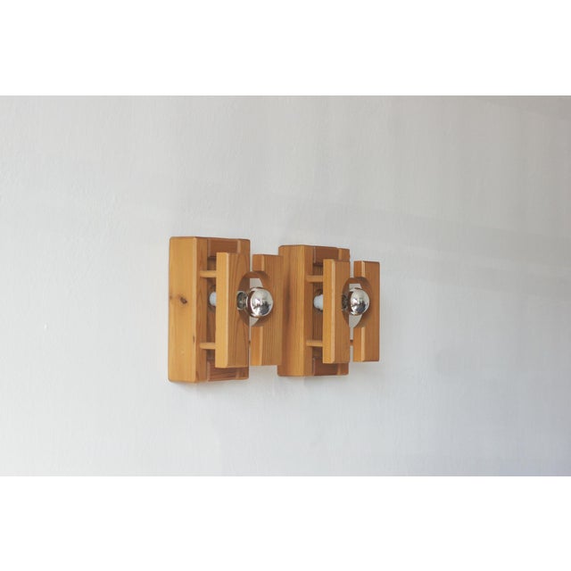 A pair of wall sconces with a geometric, architectural design, crafted from solid pine with a warm, honey-amber hue. The...