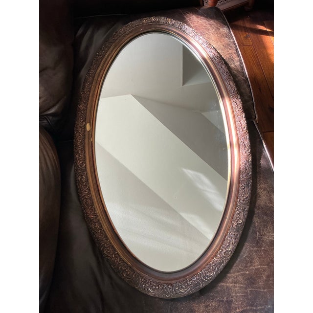 A beautifully detailed vintage oval wall mirror featuring an elaborately carved frame with flowing scrollwork, acanthus-...