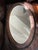 A beautifully detailed vintage oval wall mirror featuring an elaborately carved frame with flowing scrollwork, acanthus-...