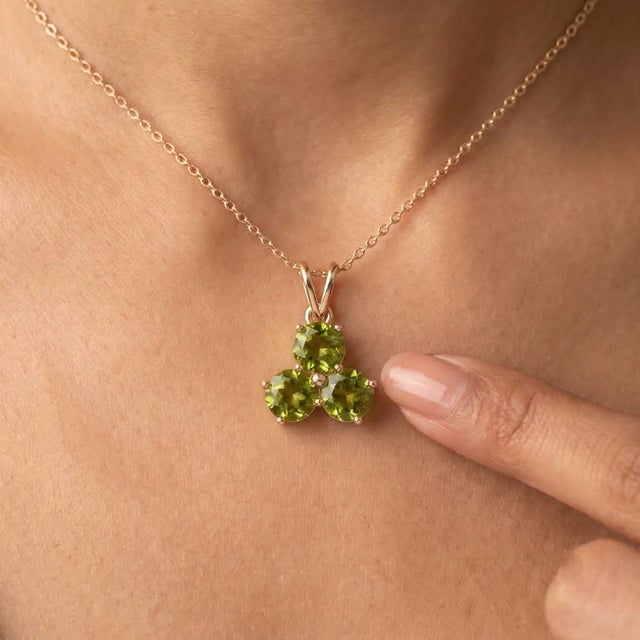 A vibrant three-stone design featuring round-cut natural peridots arranged in a graceful trefoil formation, secured in a...