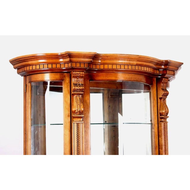 A Pulaski Furniture Company serpentine front oak curio cabinet. The cabinet has three adjustable glass shelves, and one...