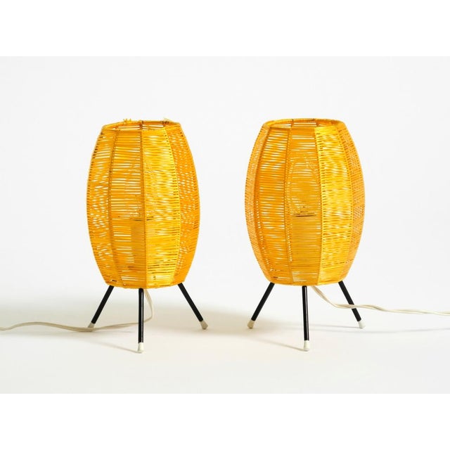 Two beautiful original Mid-Century Modern tripod table lamps. The shades are wrapped in gold-yellow synthetic raffia....