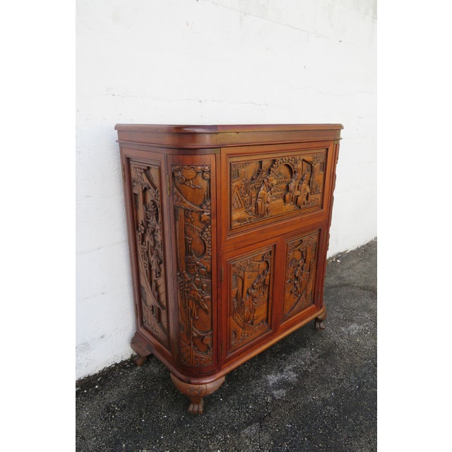 This vintage 1960s Oriental Dry Bar cabinet has heavy hand carving, it is made of solid wood, and it has light red brown...