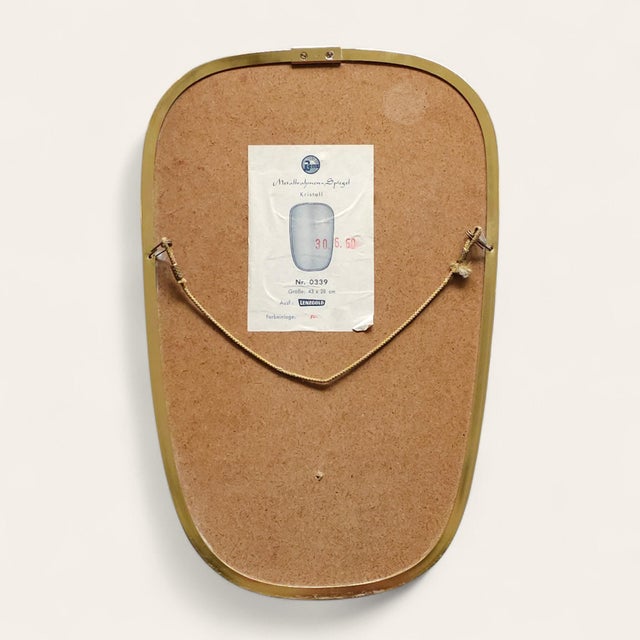 Sculptural mid-century wall mirror produced in Germany circa 1960s. The slender brass frame features a distinctive red...