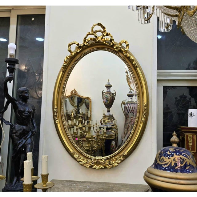 Elegant French-style oval wall mirror featuring a richly hand-carved frame with intricate ornamental detailing and a...