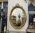 Elegant French-style oval wall mirror featuring a richly hand-carved frame with intricate ornamental detailing and a...