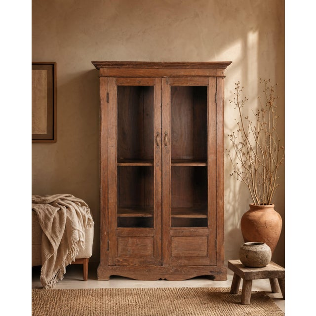 This almirah has a quieter elegance, a shaped apron at its base, carved lower door panels, and brass drop handles that...