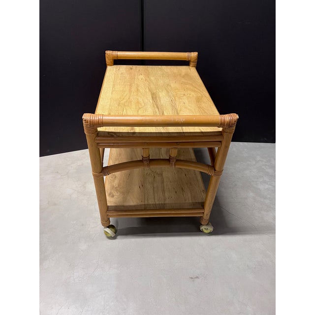 Mid Century Modern Rattan and faux wood laminate top bar cart with brass wheels. Includes lower shelf.