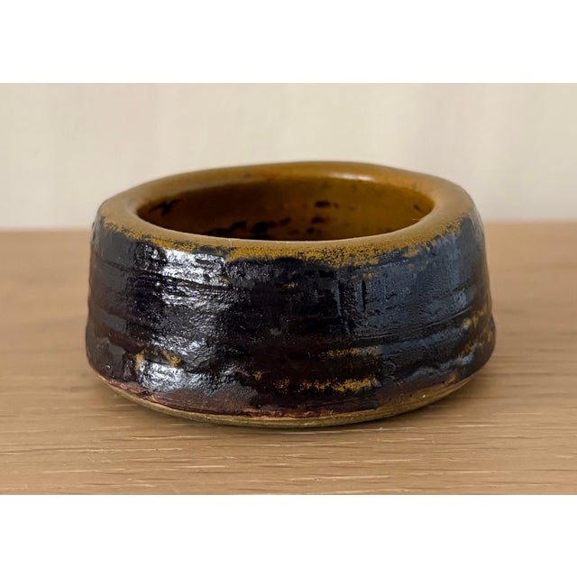 A small vintage studio pottery ring dish or pinch bowl with a low cylindrical form and richly layered earth-tone glaze....