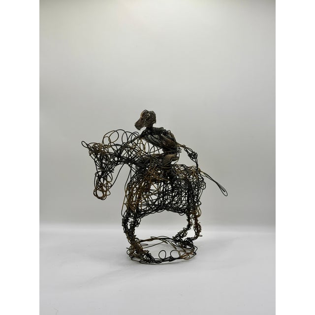 A striking vintage wire sculpture depicting a horse and rider, handmade from layered black and brass toned wire. The piece...