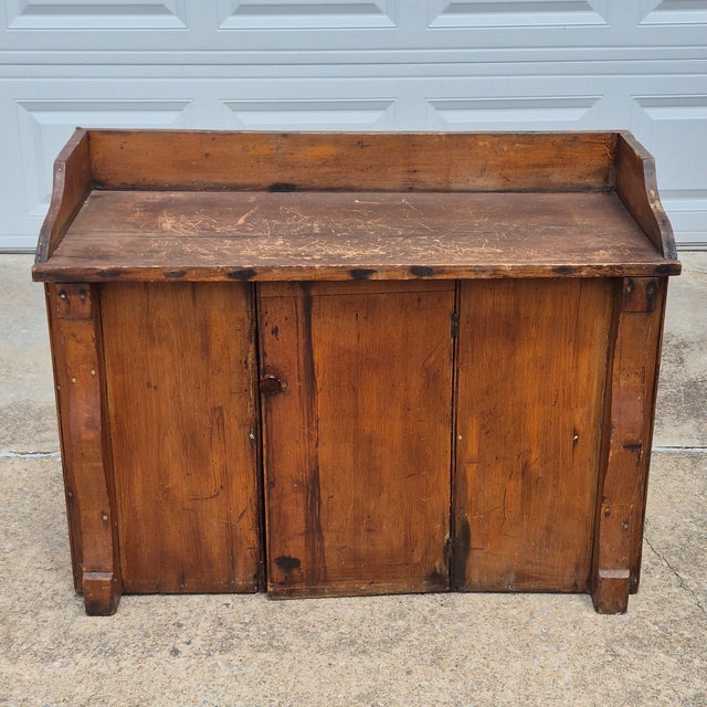 This is an antique primitive wash stand cabinet made of pine wood with a wood gallery and a single door that opens to...