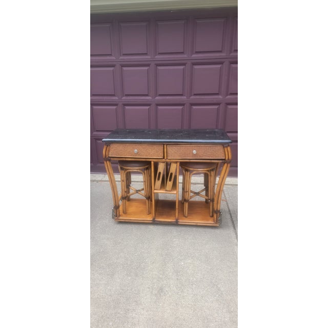 1970's vintage bamboo and rattan bar console table features a dark stone top and two woven drawers. This beautiful piece...