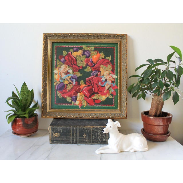 Framed vintage needlepoint wall hanging featuring a festive fruit and angel wreath. Professionally frame. Some age wear to...