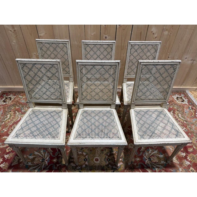 Set of six Louis XVI style chairs with square, openwork caned backs. Solid wood frames finished with a white limewash,...