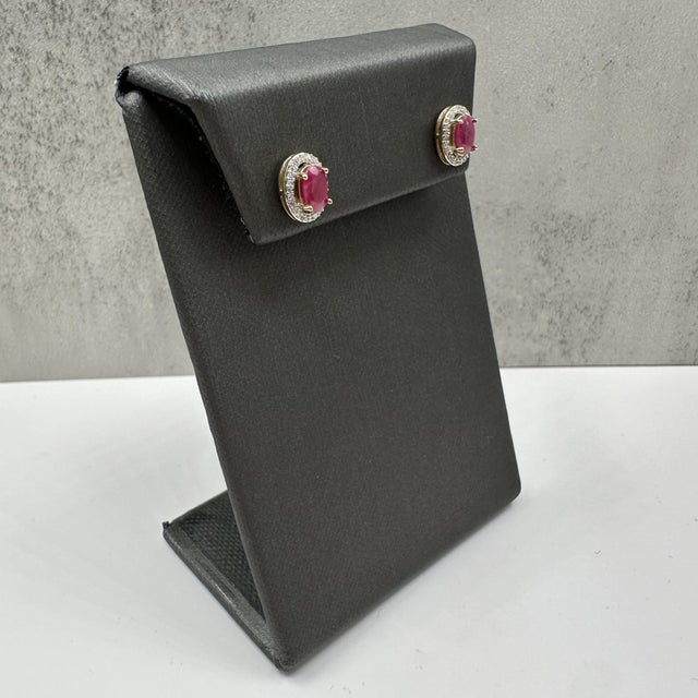 These stunning ruby and diamond halo stud earrings in 10kt yellow gold feature approximately 6x4.1mm oval cut rubies...