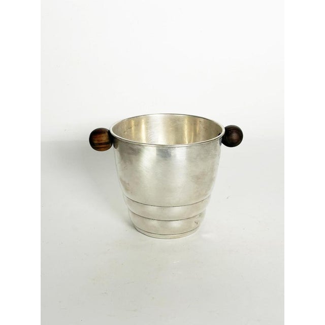 An elegant Art Deco era ice bucket crafted from silver-plated metal, featuring two spherical turned-wood handles. Its...