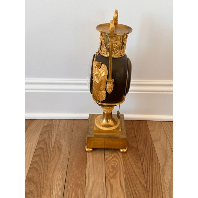 An Empire Ormolu and Patinated Bronze Urn Clock. Circa 1810. The enamelled dial with Roman and Arabic numerals signed...