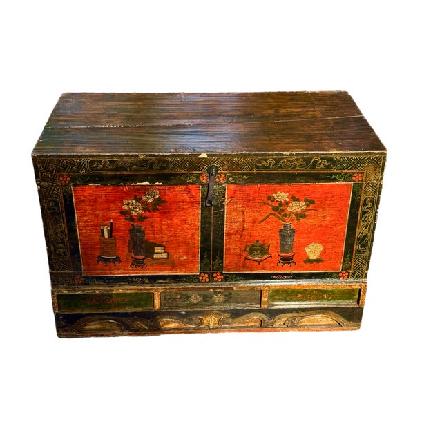A Chinese hand painted elm chest in red with Asian motifs, carved detail and stencil work. The art on the front is...