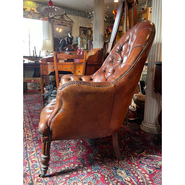 Stunning antique English library chair with gorgeous deep tufted leather, beautiful wooden legs with brass casters and...