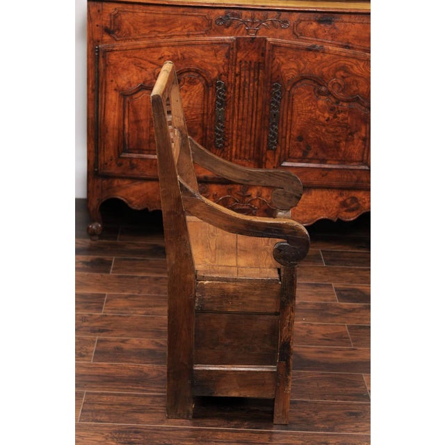 An English country pine chair from the early 19th century, with pierced back, scrolled arms and lift-top seat. This rustic...