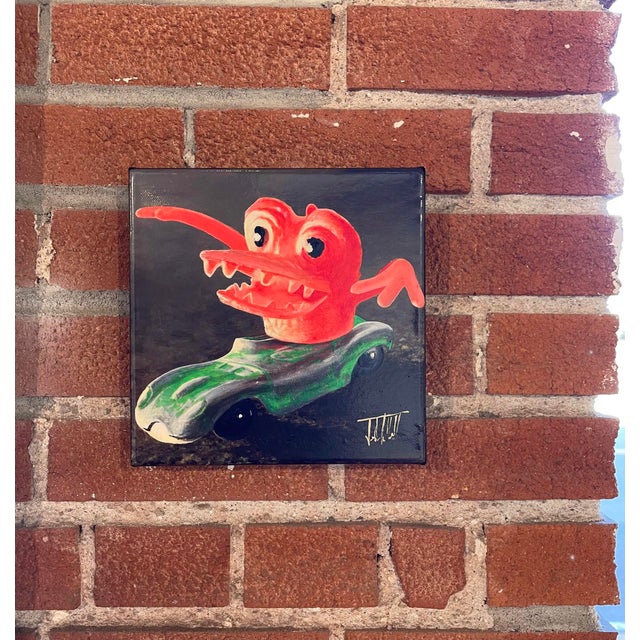 This artwork features a whimsical creature with a vibrant, orange head and exaggerated features, perched atop a green toy...