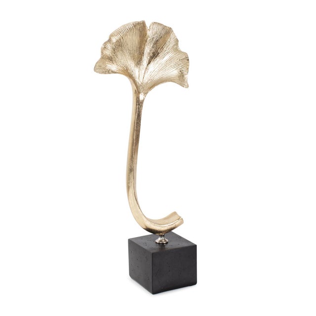 The delicate ginko leaf, finished in brushed gold texture, gracefully floats atop a sleek black base. Reflecting light...