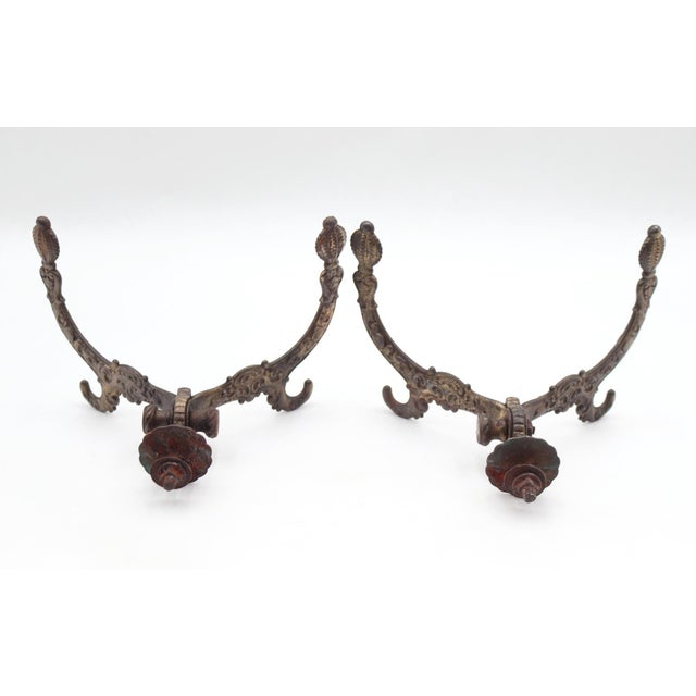 Victorian style hall tree hooks made of cast iron with a dark brass finish. There are screws attached to the backs with a...