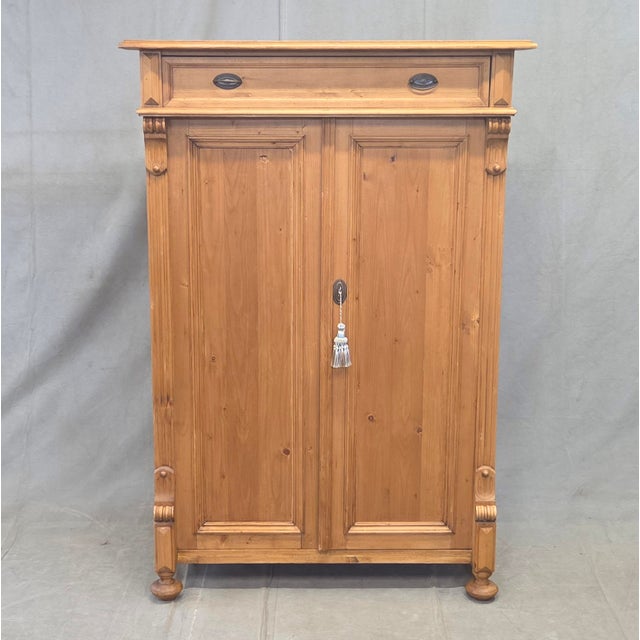 A charming and functional German natural pine tall storage cabinet with brass hardware and a working key. The clear...