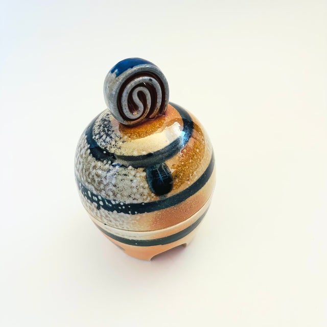 A vintage postmodern studio pottery container. Features a design of black, tan, and beige glazes around the sides. Nice...